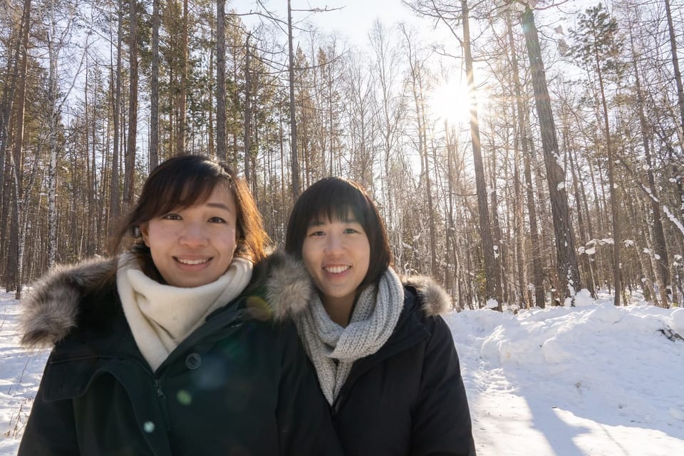 ผู้ร่วมเดินทางสองคนยิ้มในป่าสนที่มีหิมะและแสงแดด